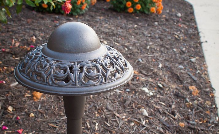 a close up of a lamp post in a garden with flowers in the background