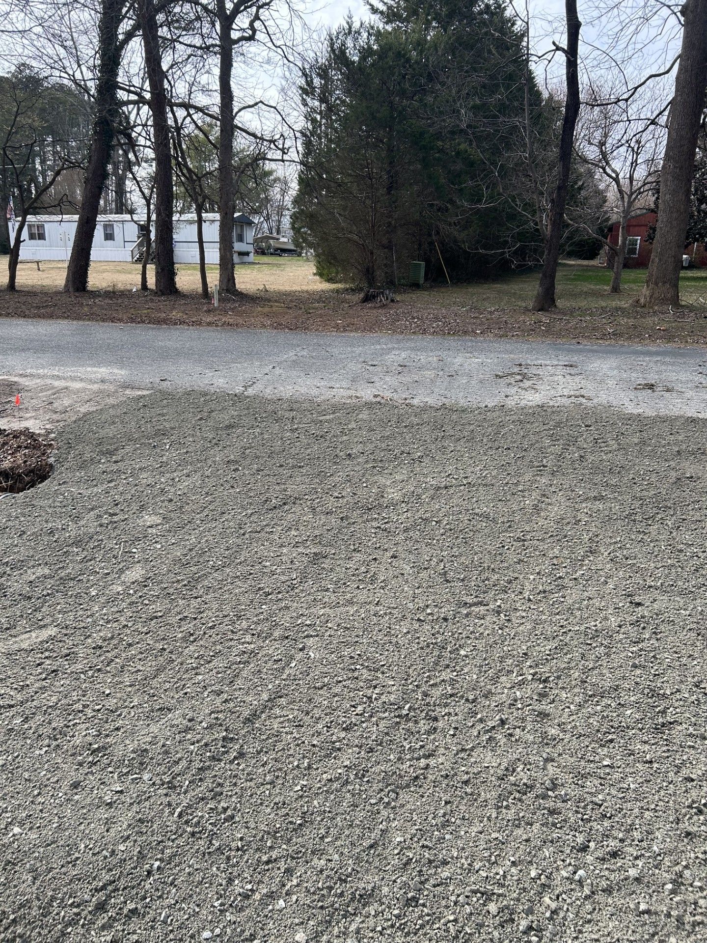 Gravel driveway leading to trees and houses in the distance. Overcast sky.