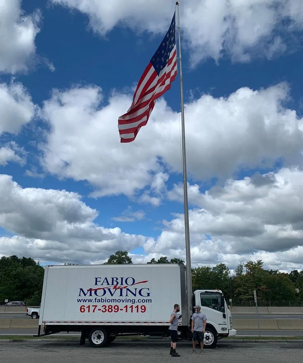Moving truck parked under an American flag; two men standing in front.
