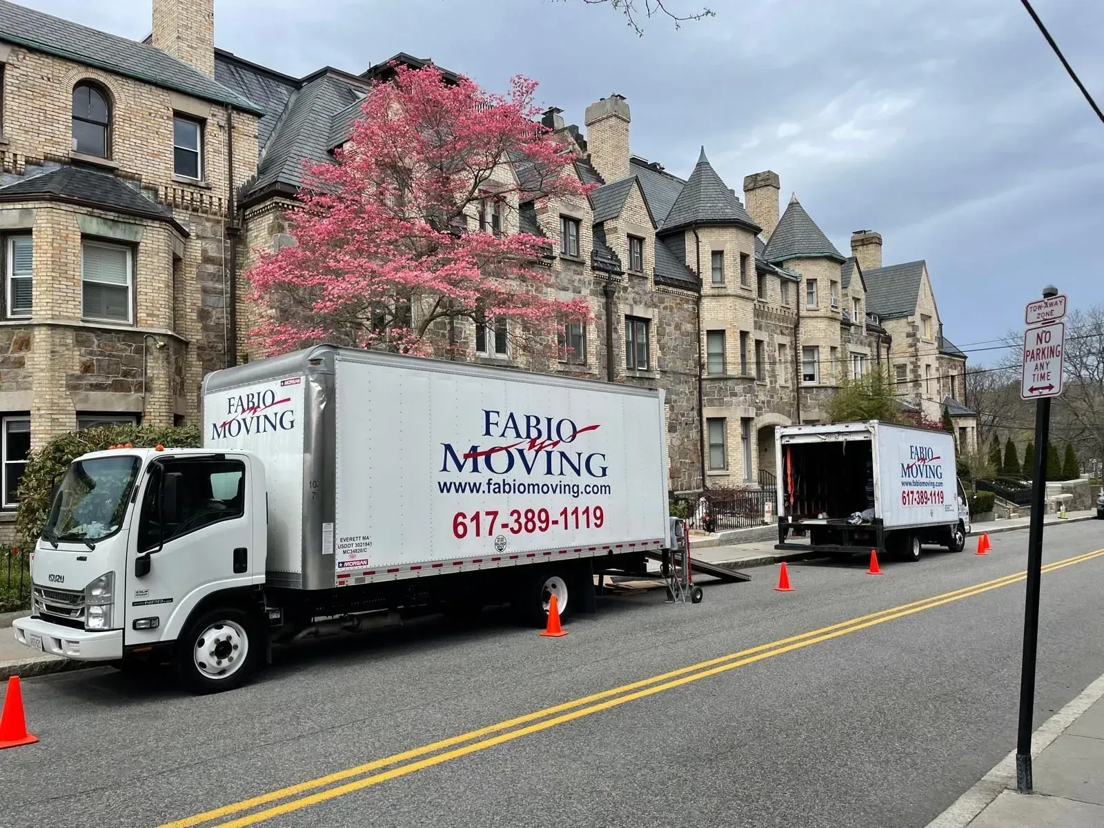 Two Fabio moving trucks parked on a street with a large brick building in the background.