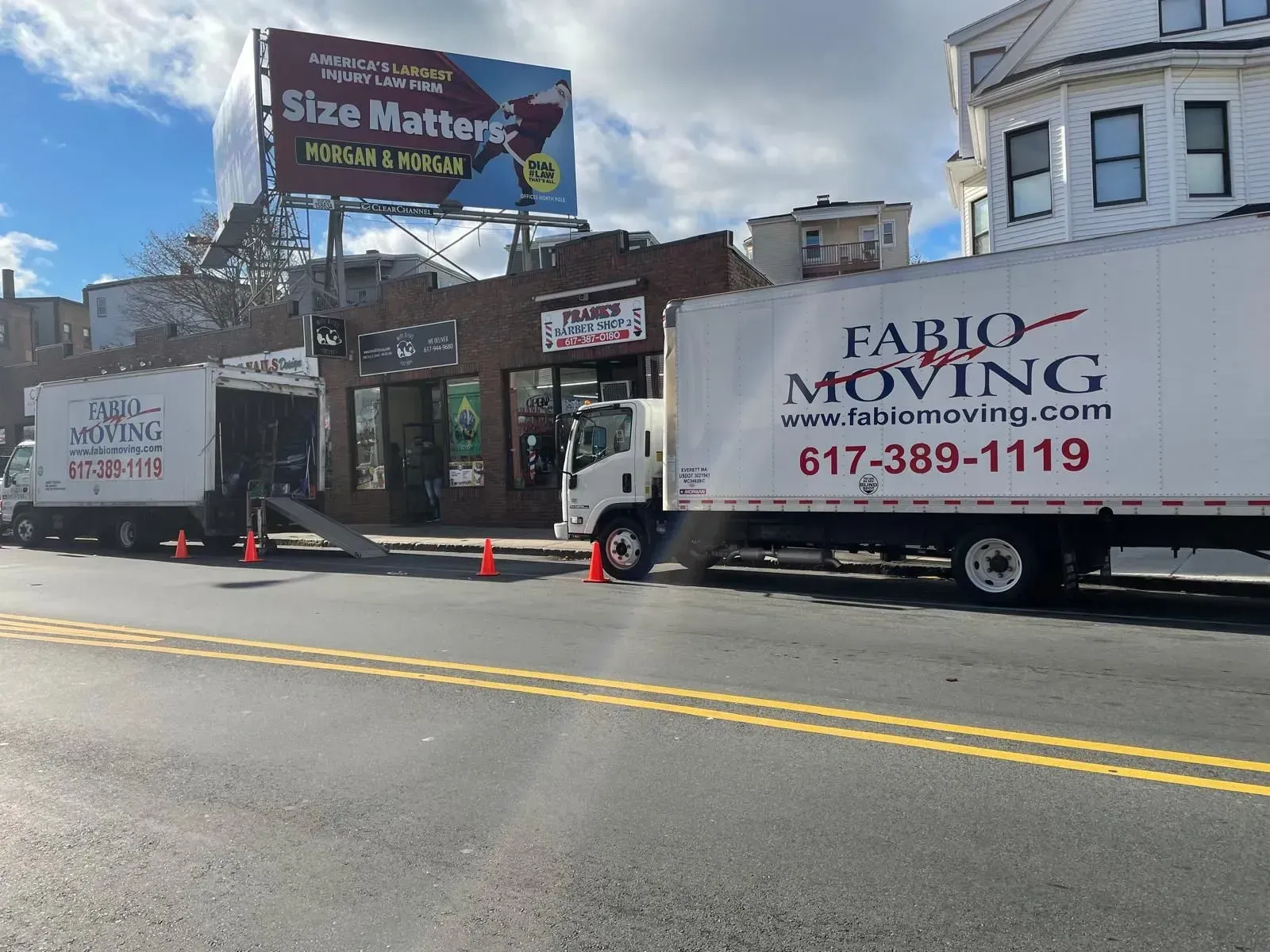 Two Fabio Moving trucks parked on street, loading near a commercial building.