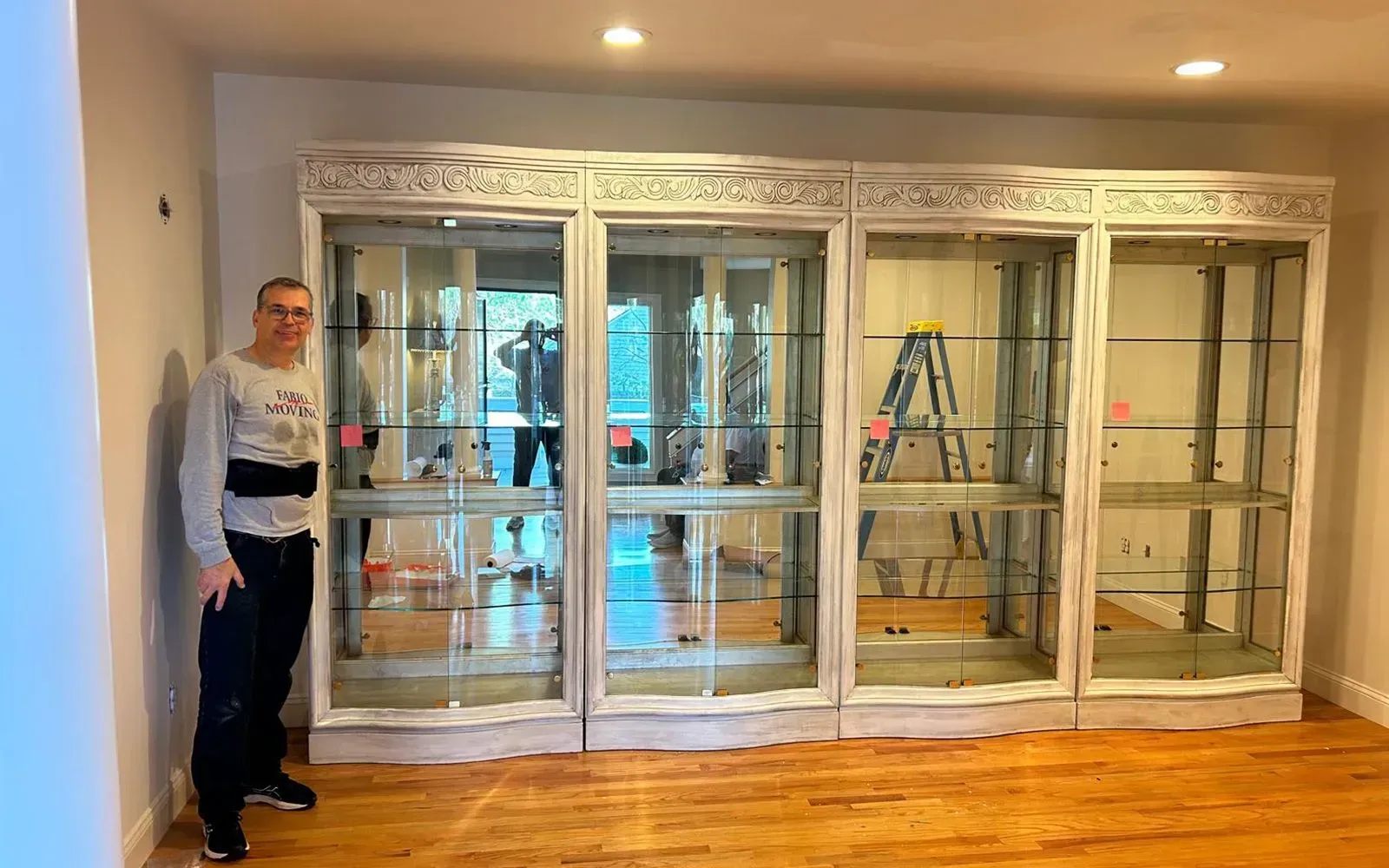 Man standing beside a large, ornate white glass display cabinet in a room with wood floors.