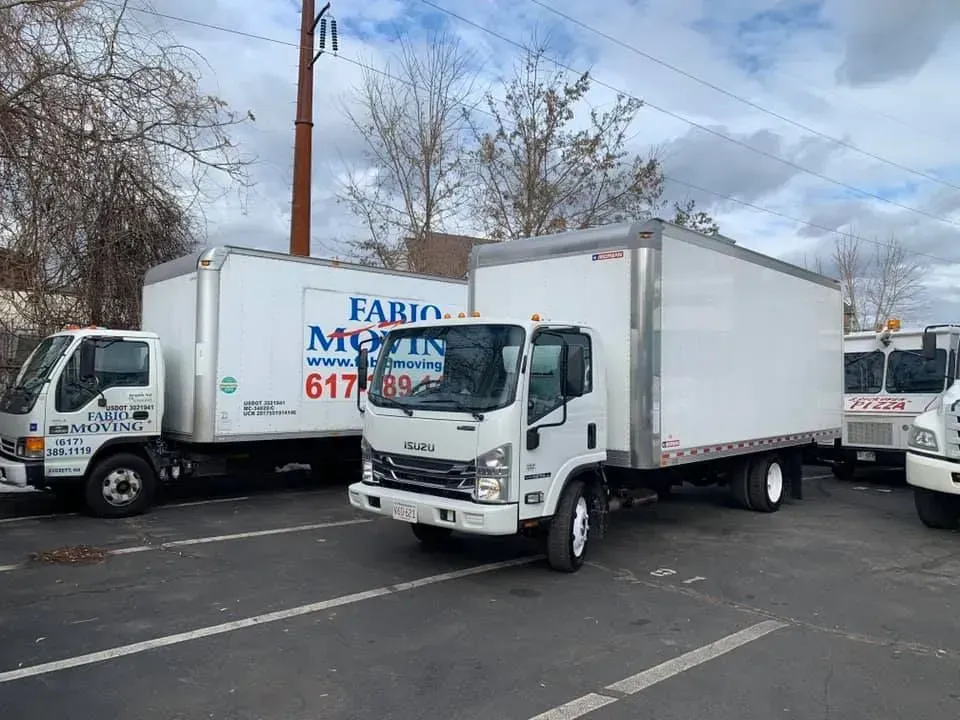 Moving trucks parked, white with company logos. Daytime, outdoors.
