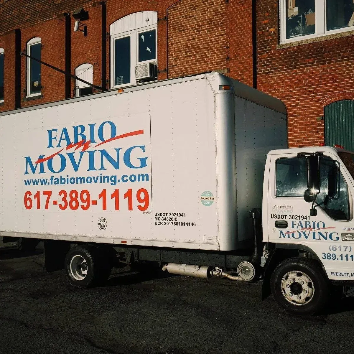 White Fabio Moving truck parked in front of a brick building; phone number is 617-389-1119.