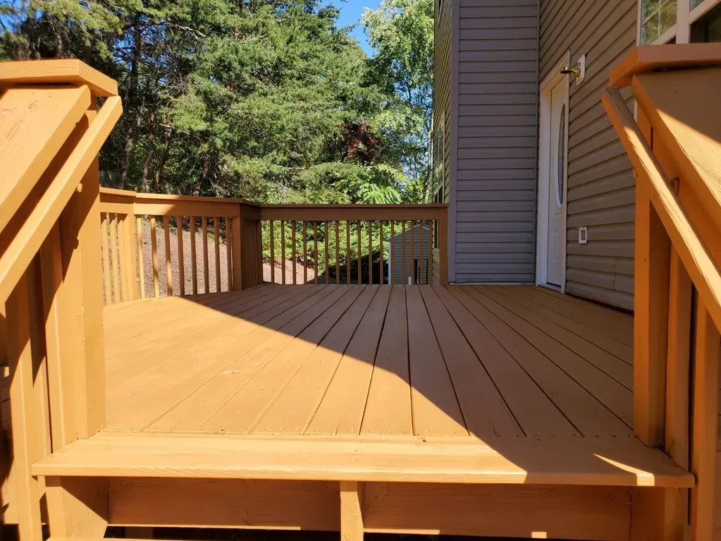 A wooden deck with stairs leading up to it is in front of a house.
