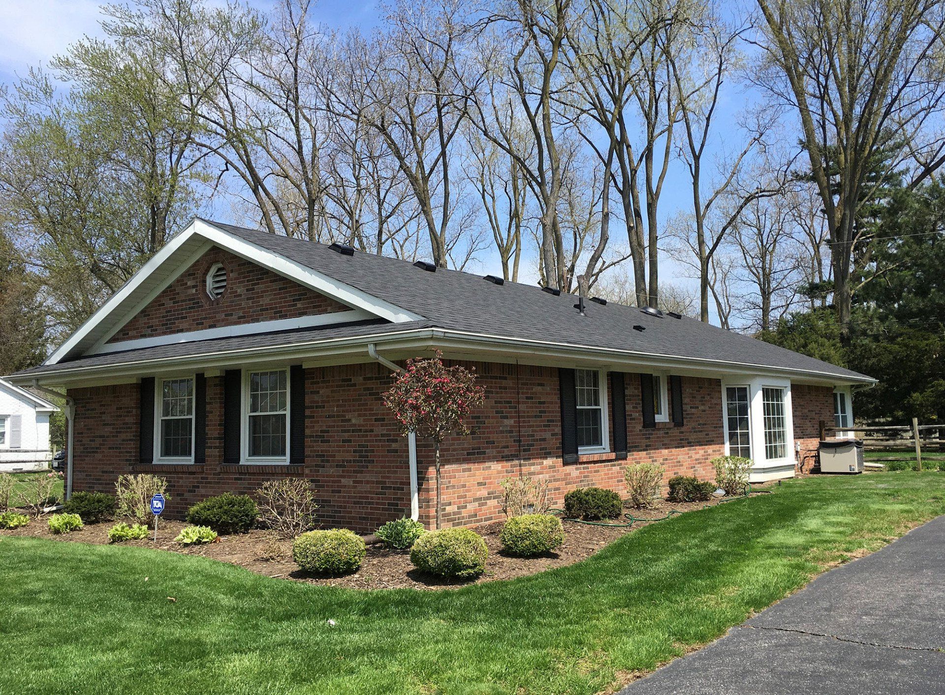 Brick ranch home with dark roof, black shutters, and landscaping on a grassy lawn.