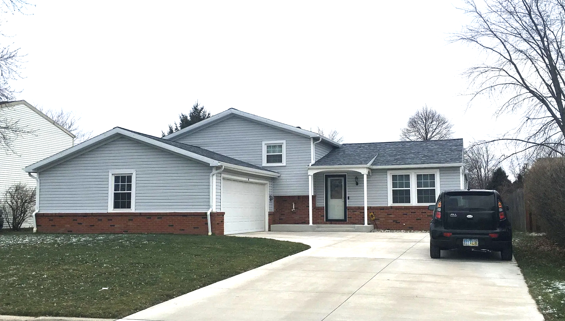 Light blue house with brick trim, garage, and a car parked in the driveway. Overcast sky.