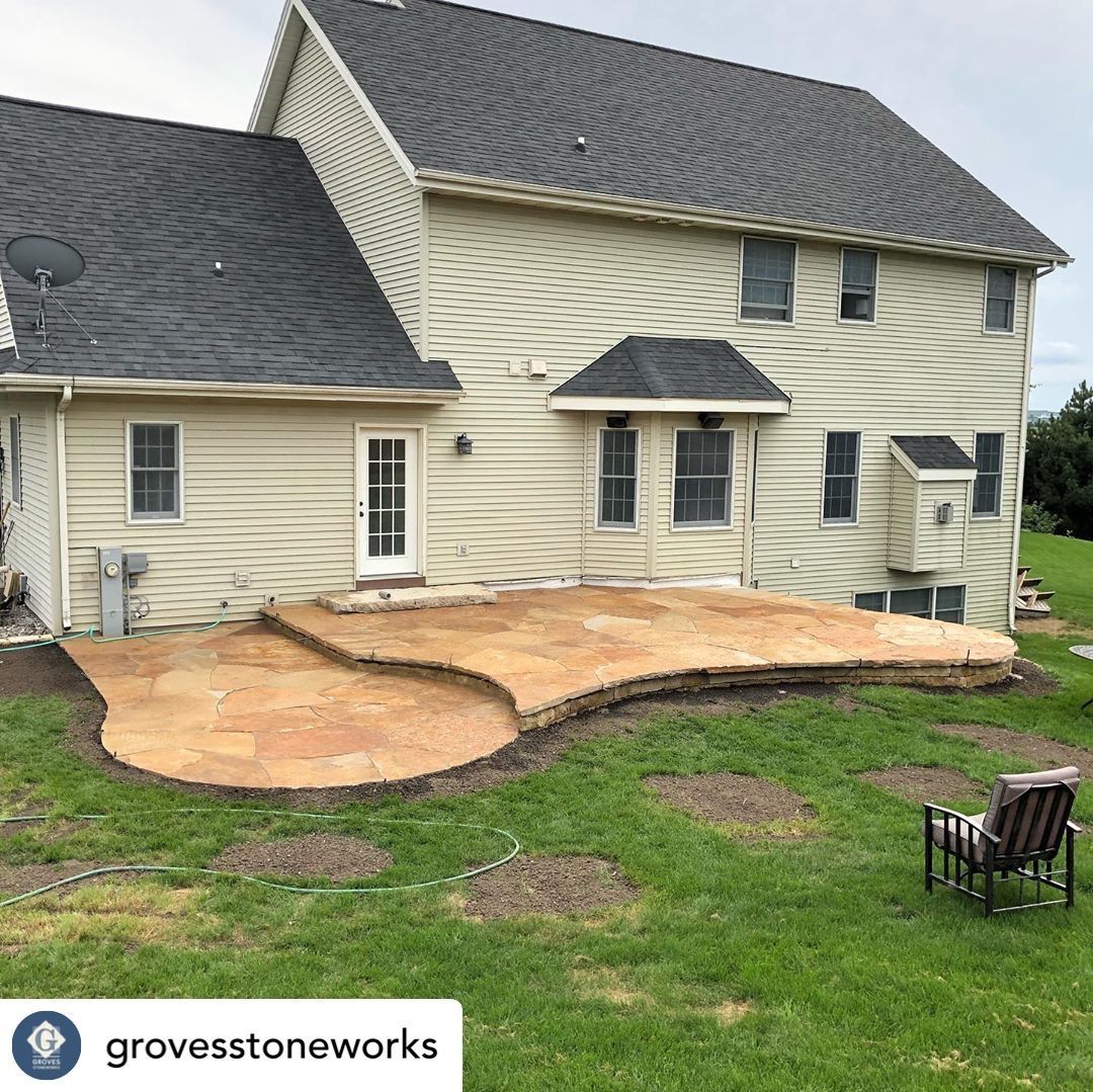 Stone patio with curved edges in a backyard setting next to a beige house.