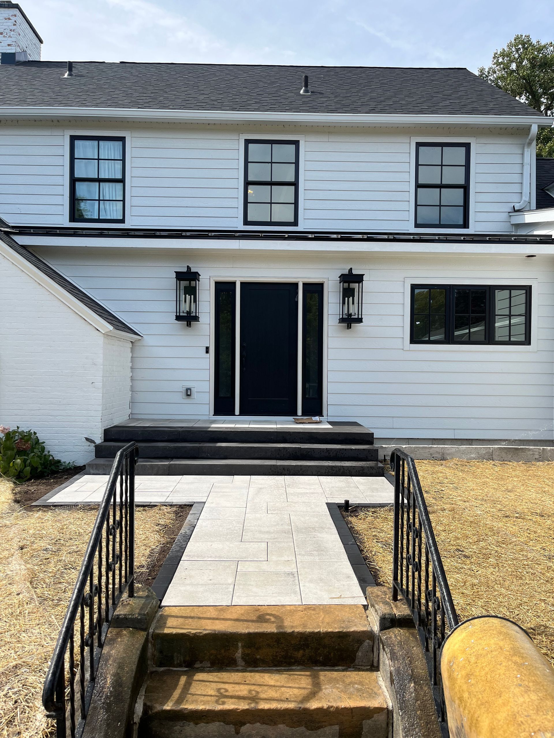 Stone patio with built-in benches, surrounded by grass and trees under a blue sky.