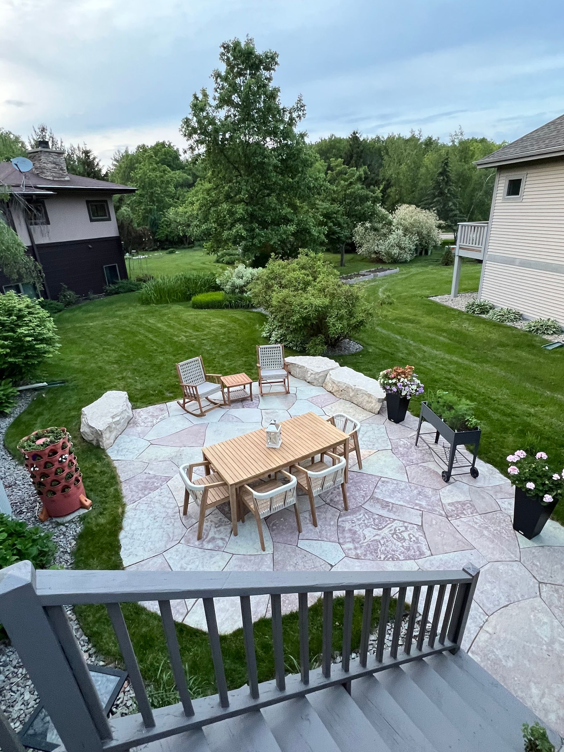 Stone patio with built-in benches, surrounded by grass and trees under a blue sky.