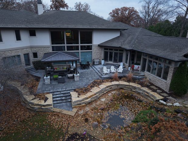 Large house with patio, landscaping, and a water feature in a natural setting.