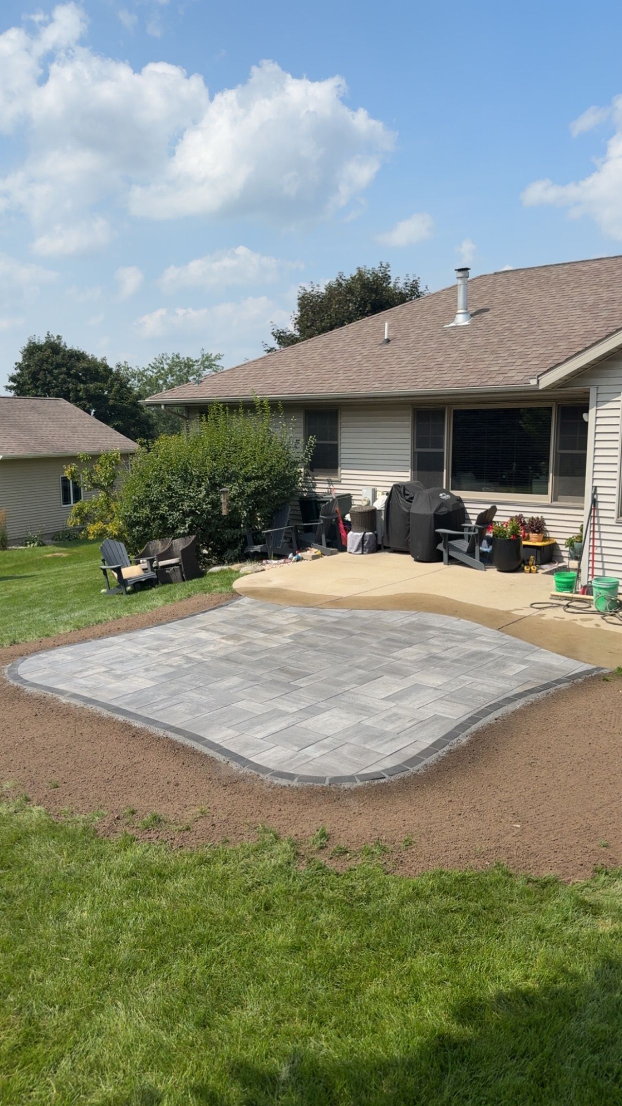 A partially constructed patio in a backyard with a house in the background and green grass surrounding it.