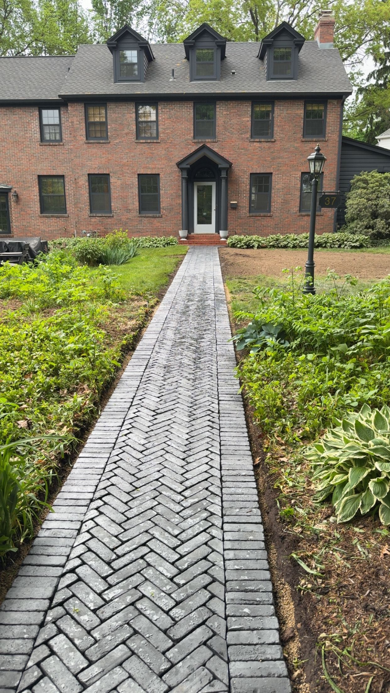 Brick house with a herringbone pattern walkway and overgrown landscaping.