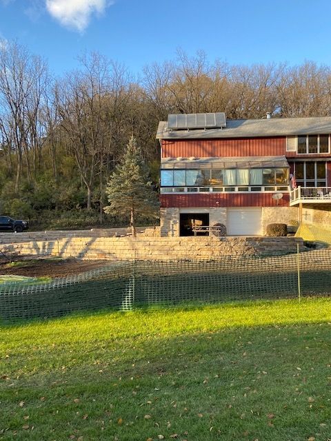 Red and white house with large windows, set against a backdrop of trees, with a grassy lawn in the foreground.