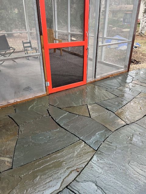 Red-framed screen door on a screened-in porch with slate patio tiles, wet from rain.