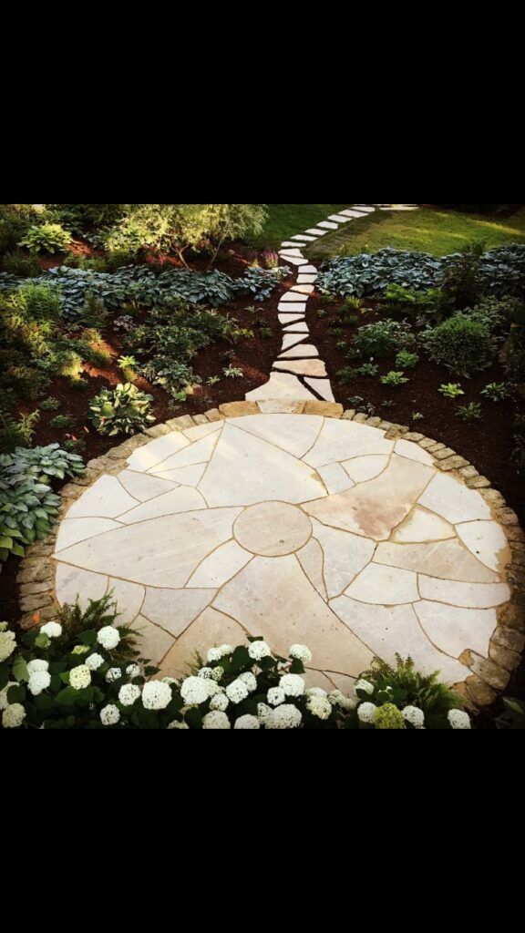 Circular stone patio surrounded by greenery and leading to a winding stone path.