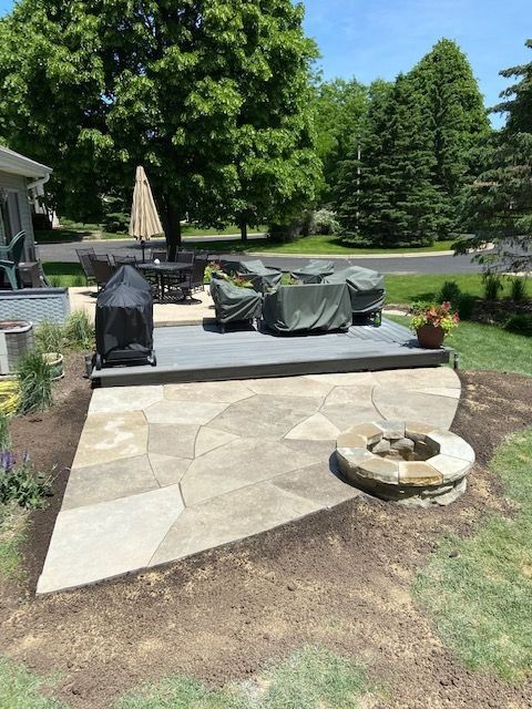 Patio with stone pavers, covered outdoor furniture, grill, fire pit, and surrounding greenery.