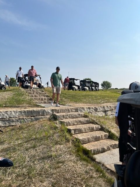 People walking on stone steps near golf carts on a sunny day.