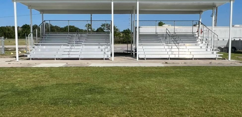 Two white bleachers are sitting on top of a lush green field.