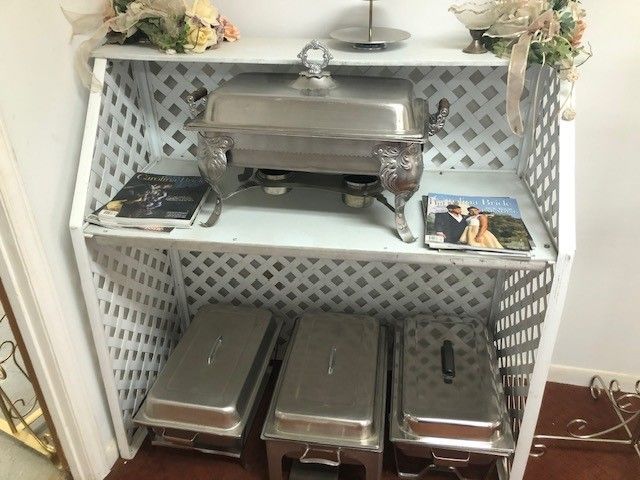 White latticework buffet table with silver chafing dishes and floral decorations.