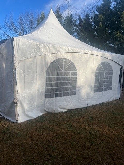 White outdoor party tent on brown grass, blue sky in the background. Two arched windows visible.