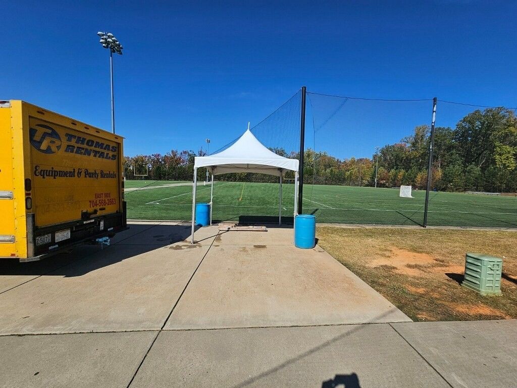Yellow truck and white tent on concrete path next to a green field under a clear blue sky.