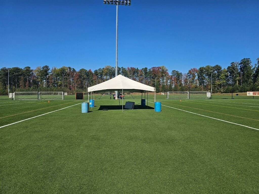 A white canopy on a green artificial turf field with a bright blue sky.