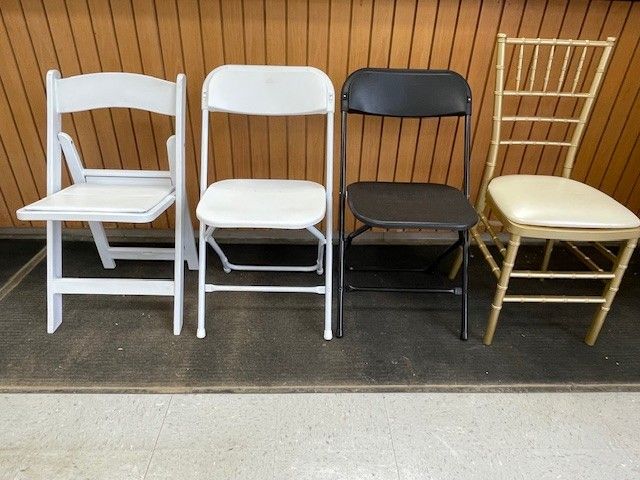 Four folding chairs of different styles and colors arranged against a wooden background.