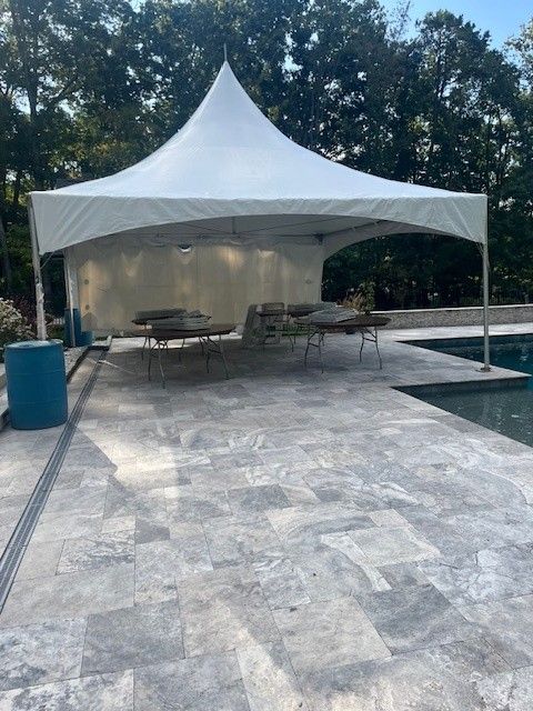 White tent over patio with gray stone flooring, pool in background.