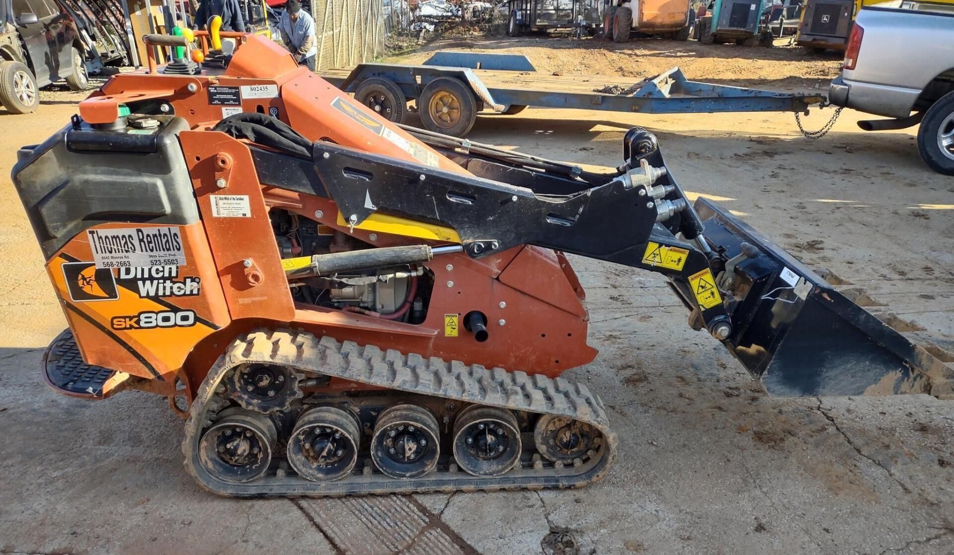 Orange and black Ditch Witch SK600 mini skid steer with bucket attachment on a gravel lot.