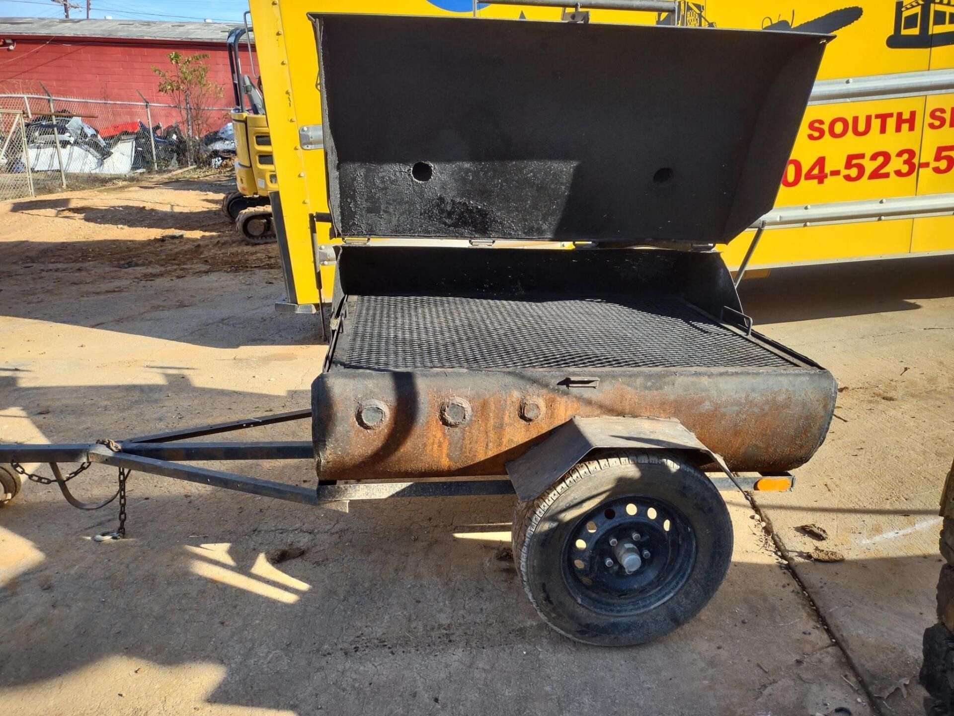 A rusty, yellow trailer with a black grill on it, parked outside.