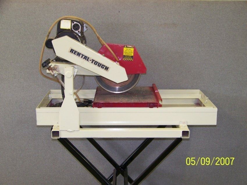 White and red tile saw on a black stand, with a water tray and a safety guard.