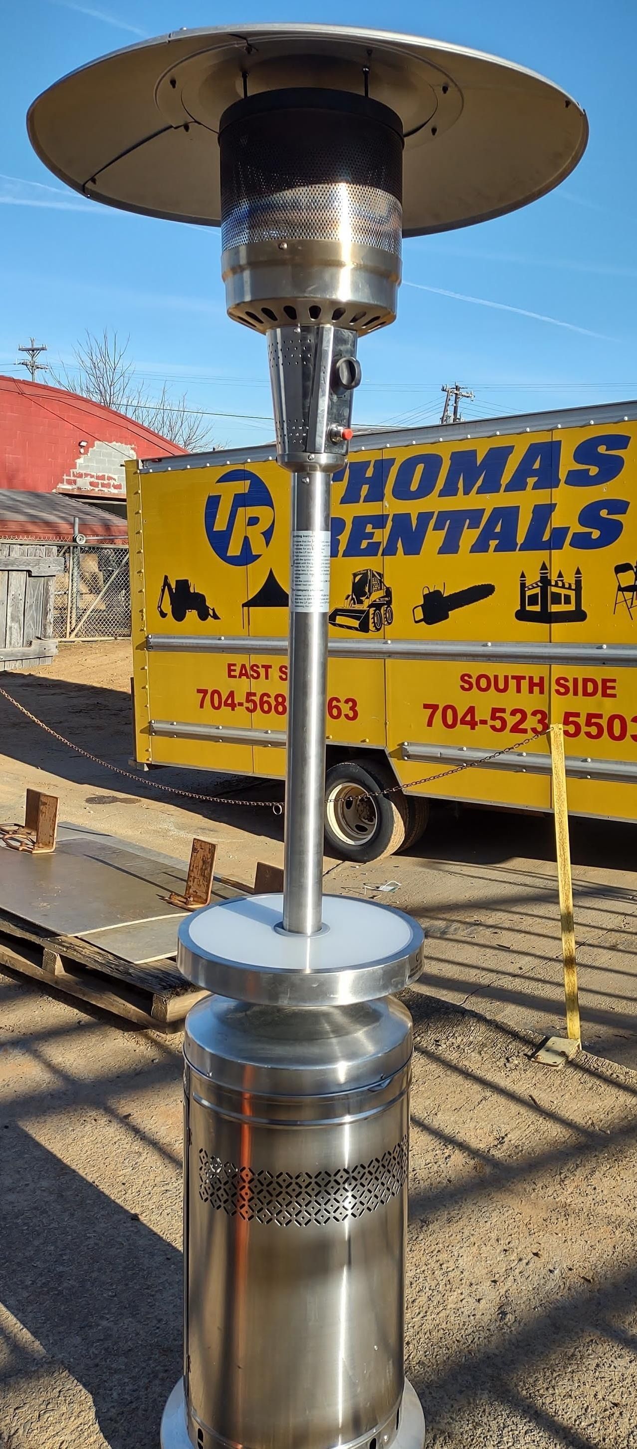 A stainless steel outdoor propane patio heater, sunny outdoor setting, yellow rental truck in the background.