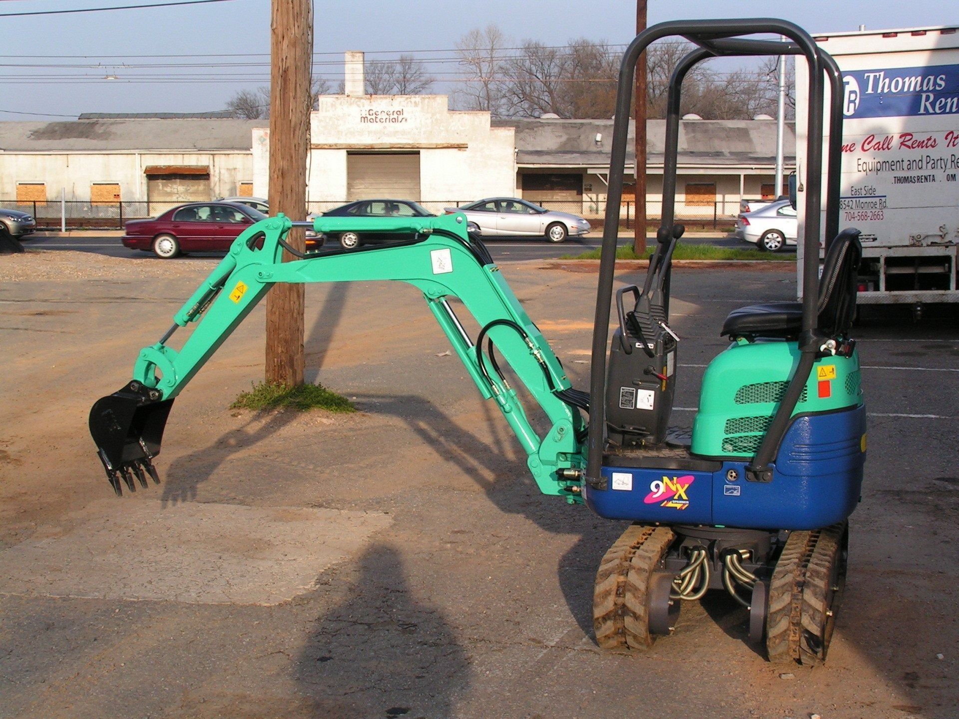 Mini excavator, teal and blue, parked on asphalt, outdoor setting.