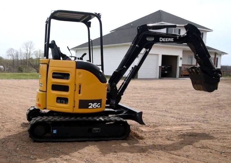 Yellow John Deere 26G mini excavator on a gravel surface in front of a house.