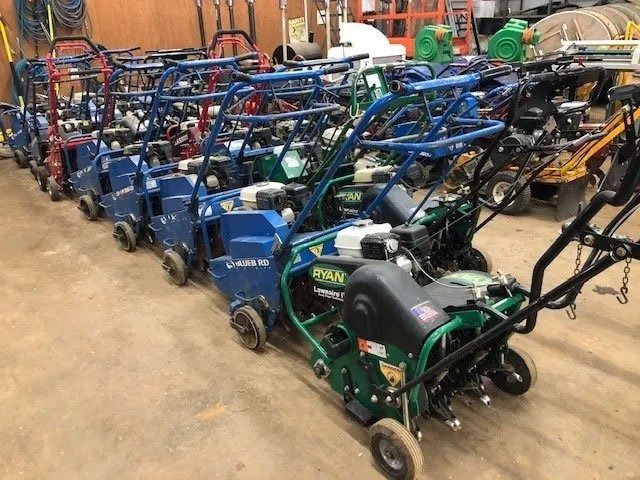 A row of Ryan lawn aerators in a storage space. They are various colors and are ready for use.