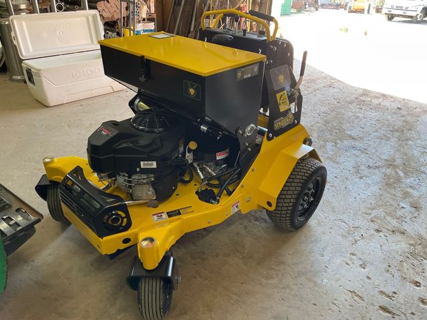 Yellow and black turf aerator machine with a black engine and wheels, parked inside.