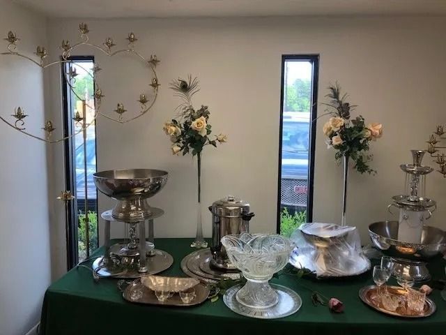 Buffet with silver serving dishes and tall flower arrangements on a green tablecloth.