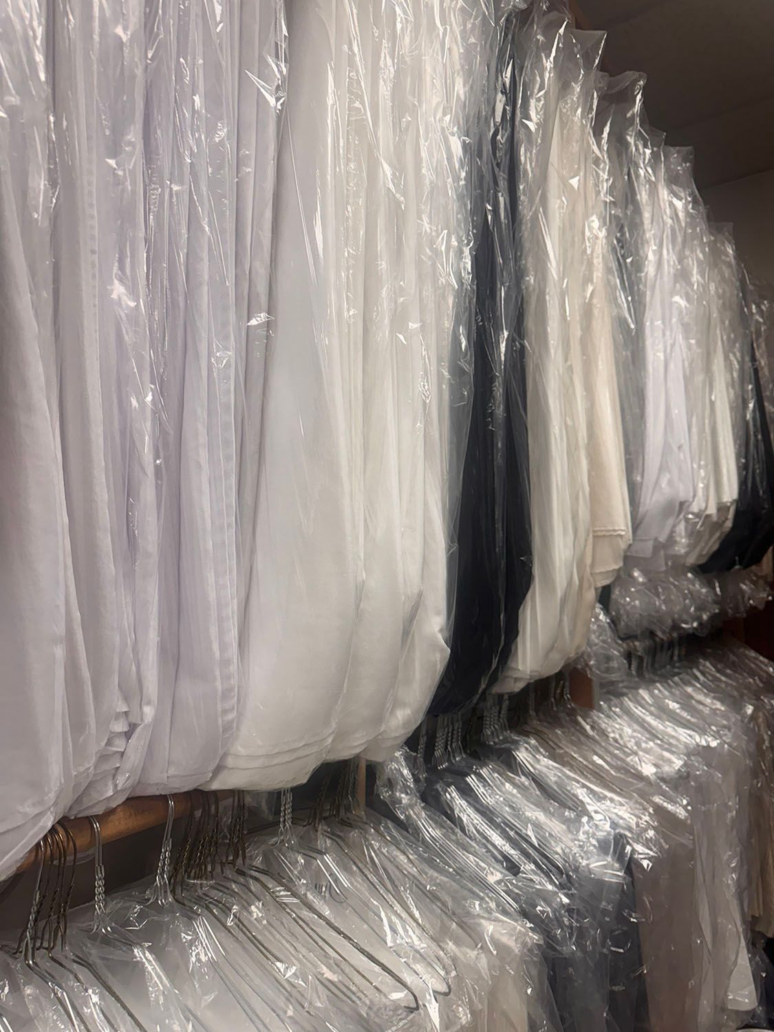 Clothes in plastic garment bags hanging on a rack.
