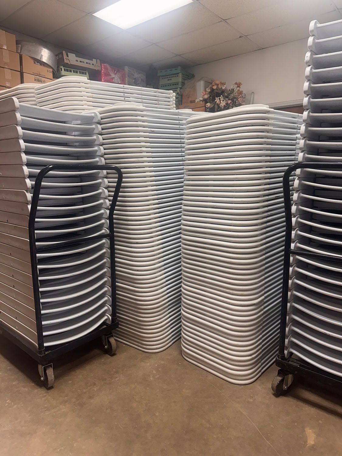 Stacks of gray metal chairs on wheeled carts in a storage room.