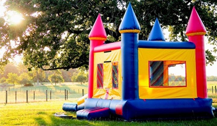 Colorful inflatable castle bounce house on a grassy field with a large tree in the background.