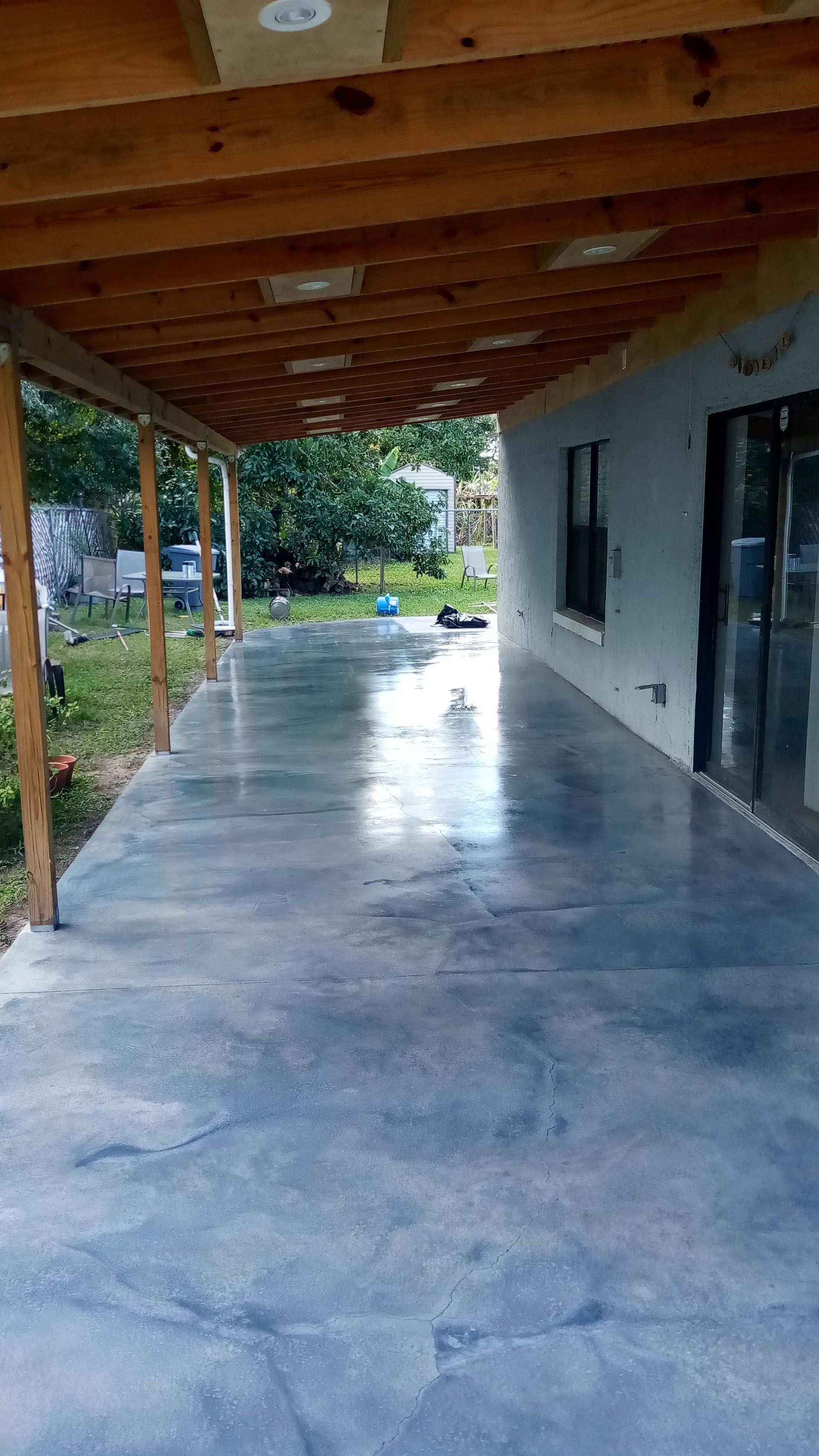 Covered concrete patio with wooden beams and a glass sliding door.