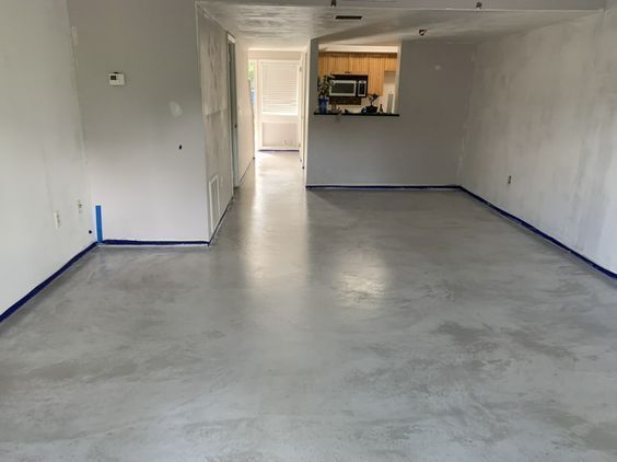 Newly finished, light gray concrete floor in an empty room, with white walls and blue tape along the edges.