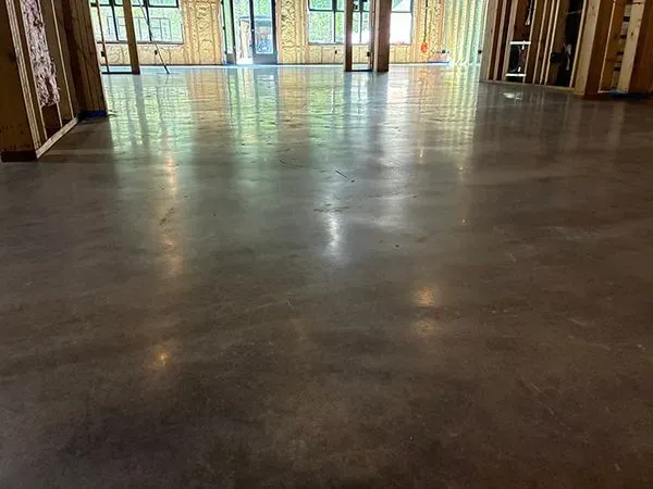 Polished concrete floor in a building under construction, reflecting the room's unfinished wooden frame and sunlight.