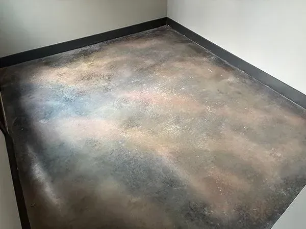 Metallic-effect concrete floor in a corner, with black trim, displaying iridescent colors like blue, gold, and pink.