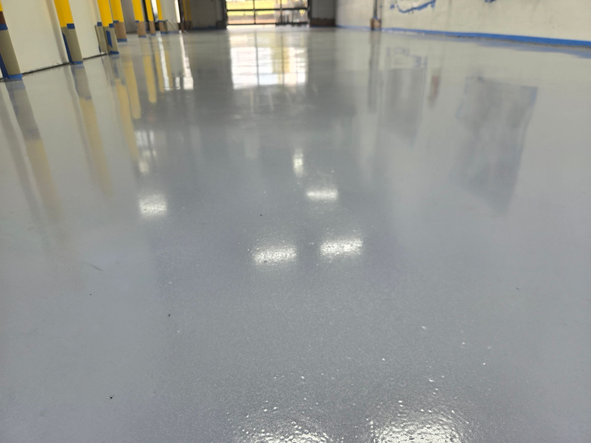 A shiny, gray, epoxy-coated floor reflecting lights in an empty room.