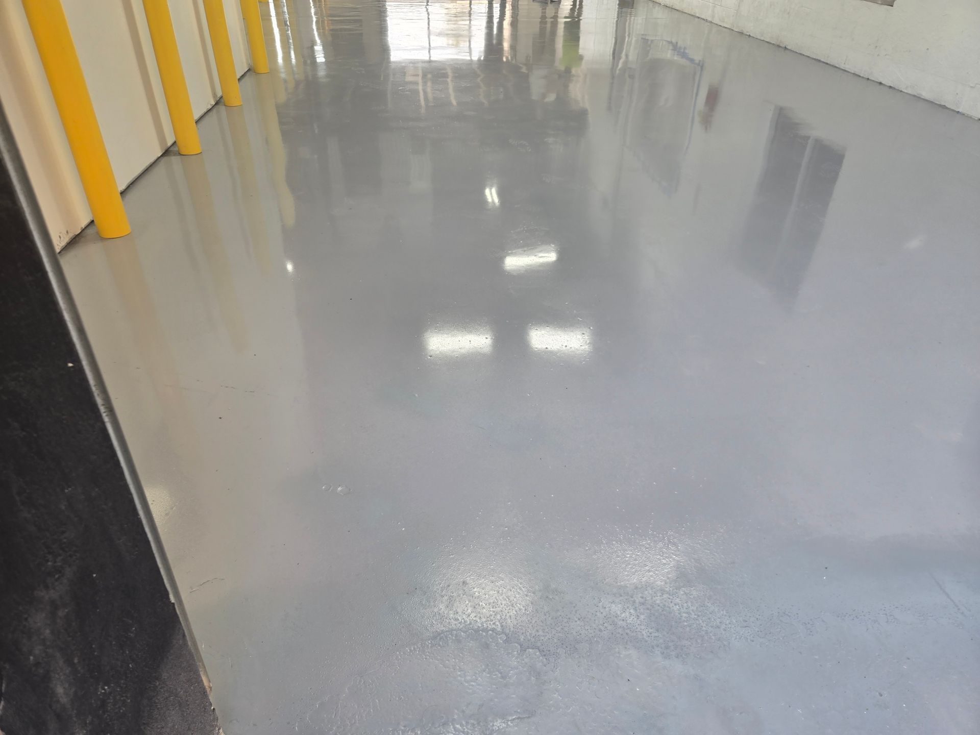 Gray, glossy epoxy floor reflecting overhead lights in a warehouse.