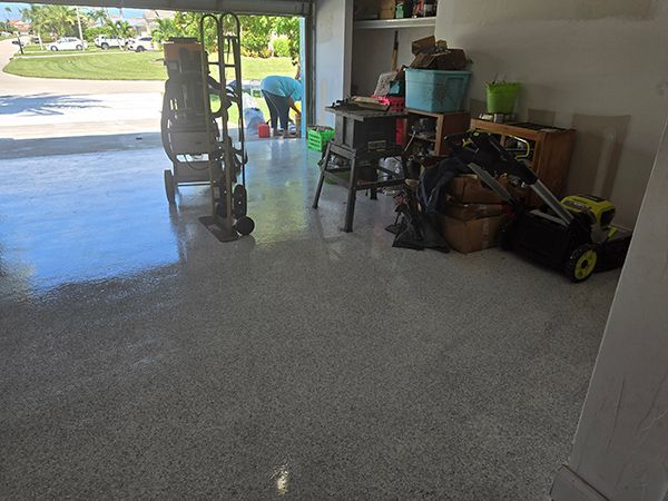 Garage with a shiny, speckled gray floor. Tools, boxes, and a person are visible.