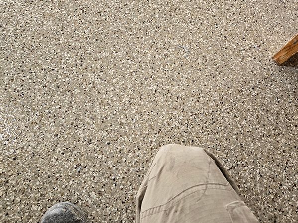 Person's legs and feet on speckled concrete floor, wearing tan pants.