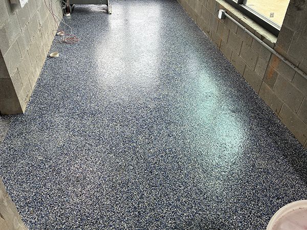 Blue speckled epoxy floor in a corridor, lit by a window. Gray cinder block walls.